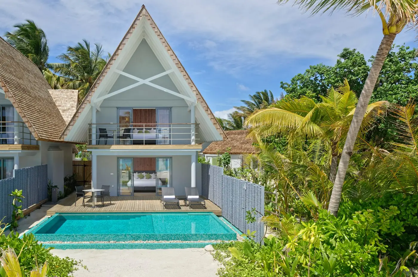 The 2-storey Two Bedroom Beach Villa, with its pointed roof, balcony and long pool in front, among the palms.