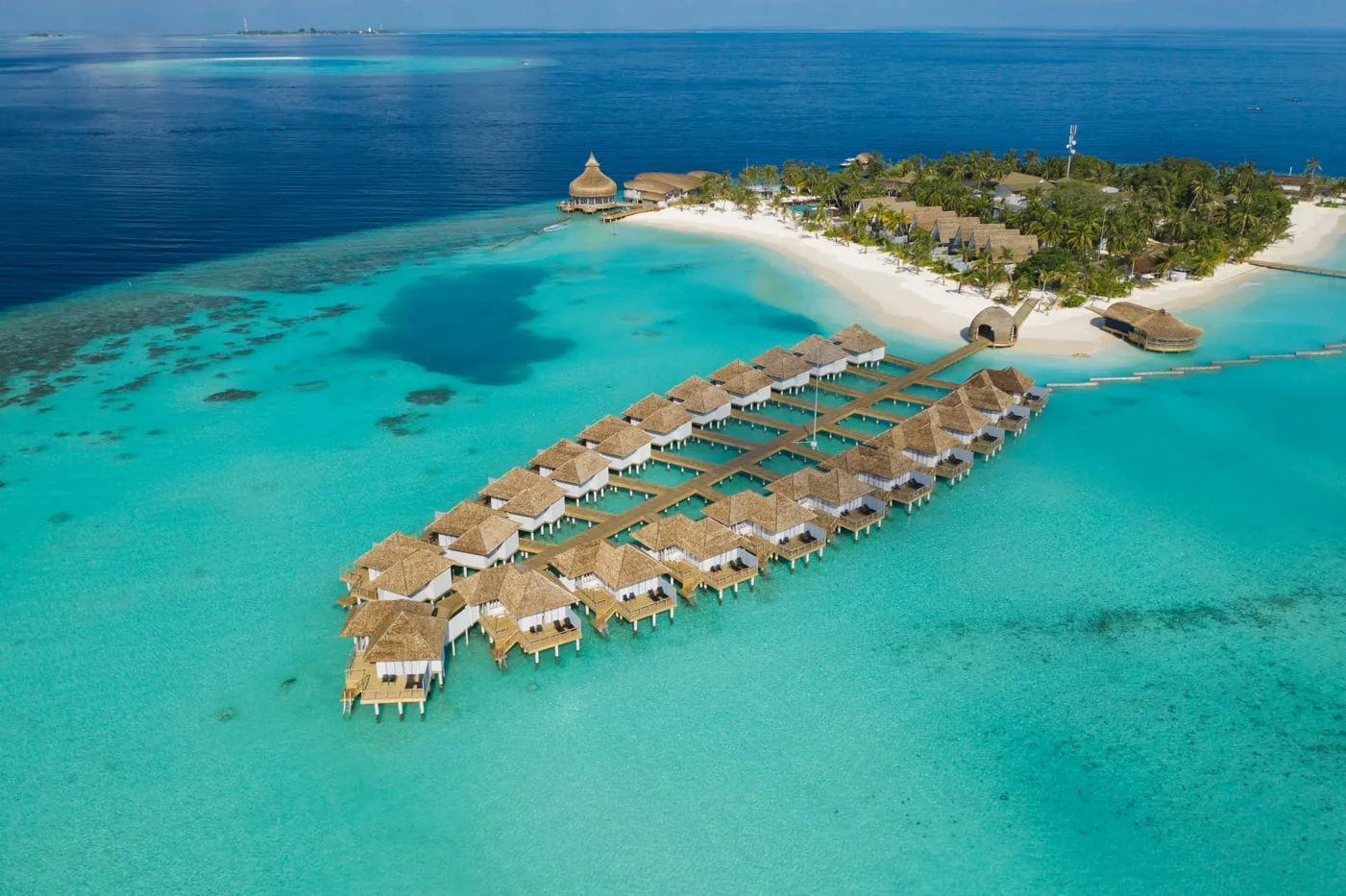 The island from above: the long horseshoe jetty of the water villas, the beach and the dense green.