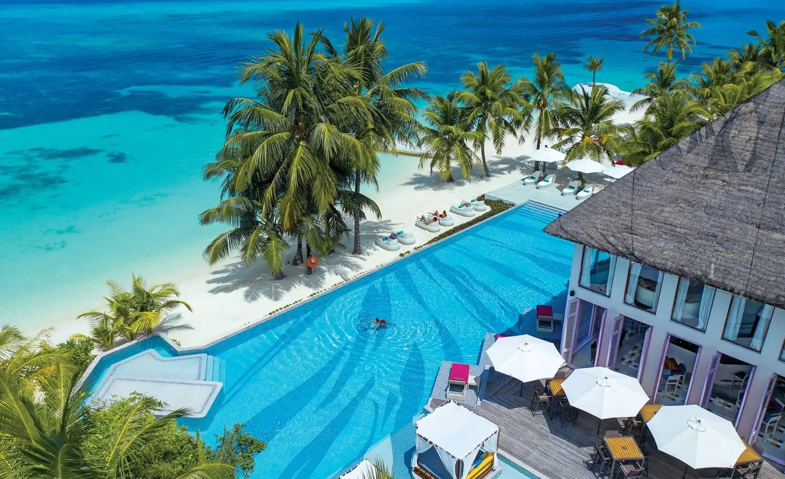 The JOIE de VIVRE pool from above, between the palms, the beach and the bar’s white parasols.