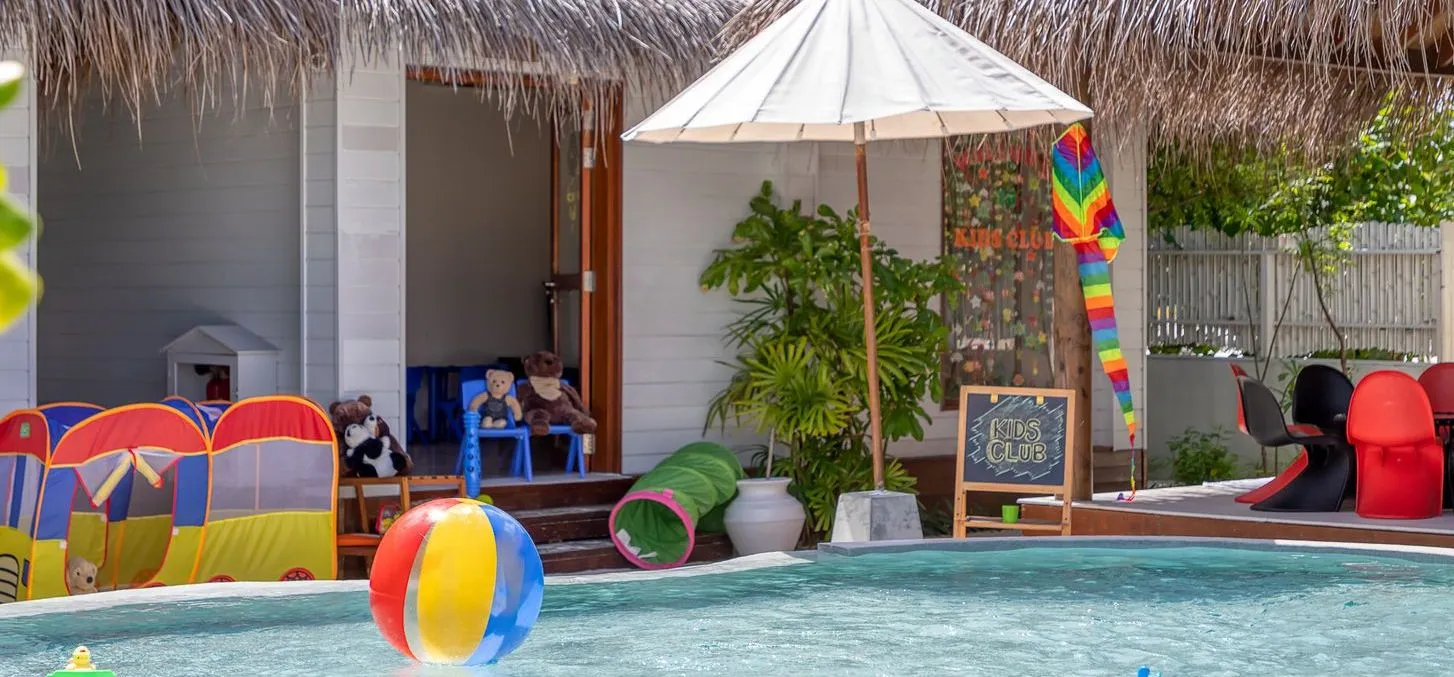 The shallow pool of the OZEN Kids Club, with coloured toys, a parasol and the thatched playhouse.