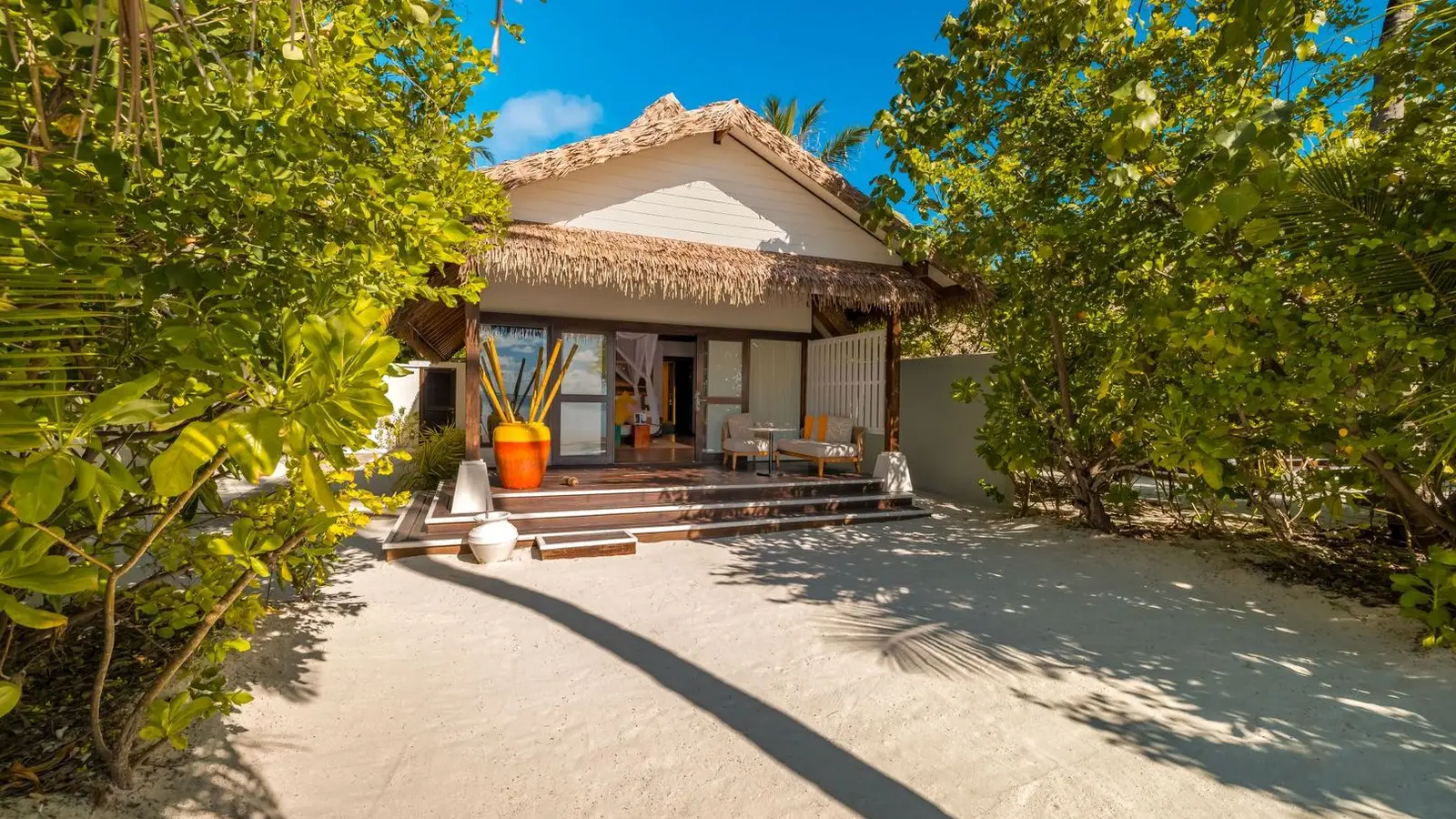 An Earth Villa on the beach: the thatched villa among the trees and its sandy path.