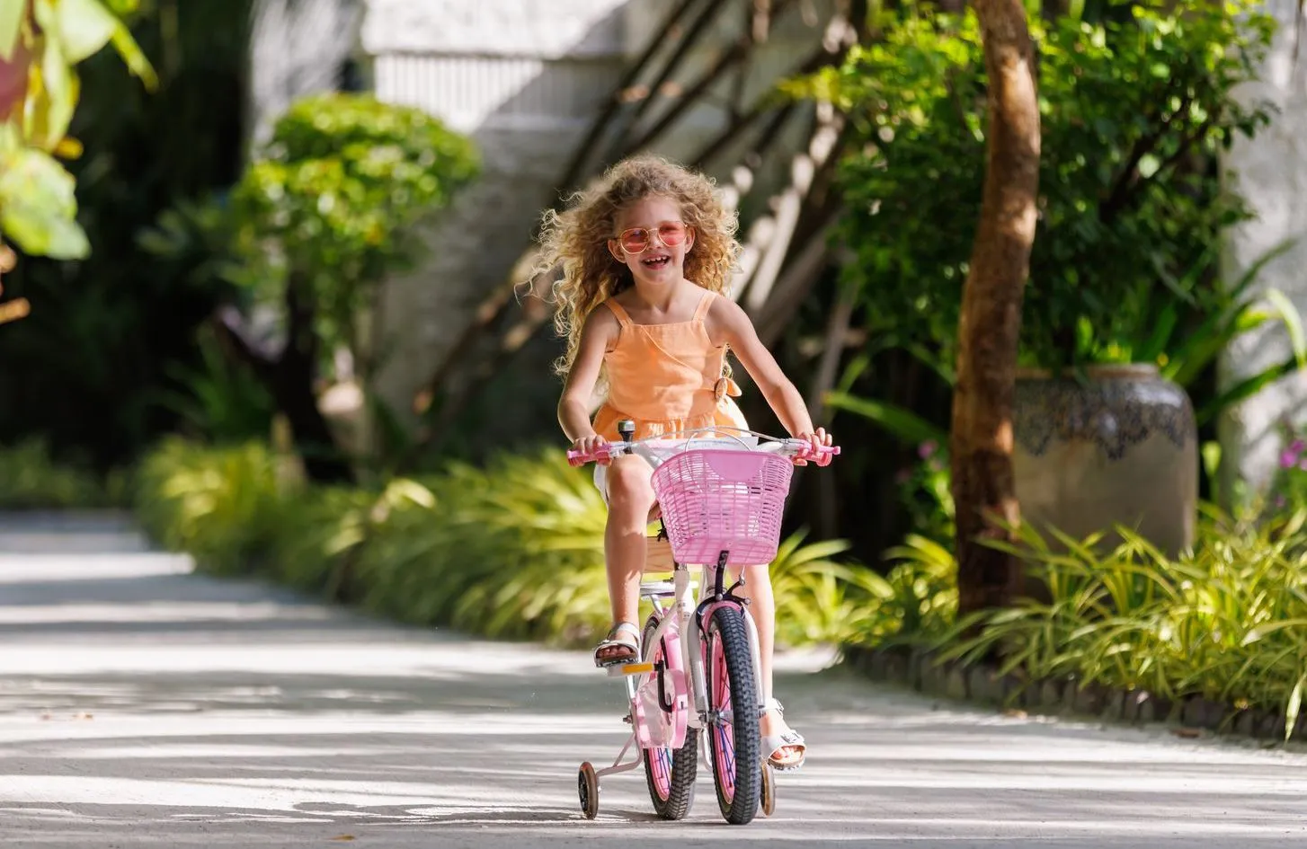 A girl smiling on a pink bicycle on one of the island’s paths, among the greenery.