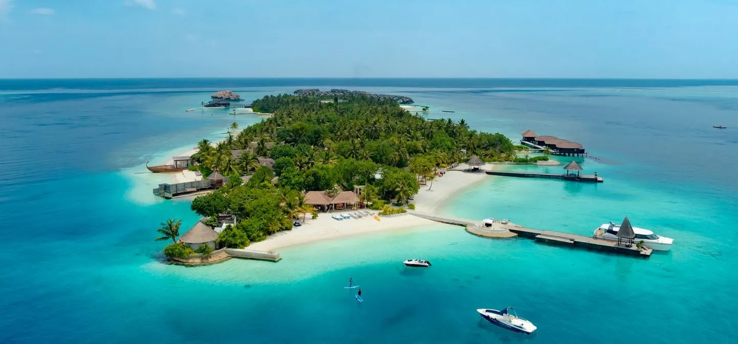 Bolifushi from above: the island under its palms, the pale beach, the jetties and the water villas at either end.