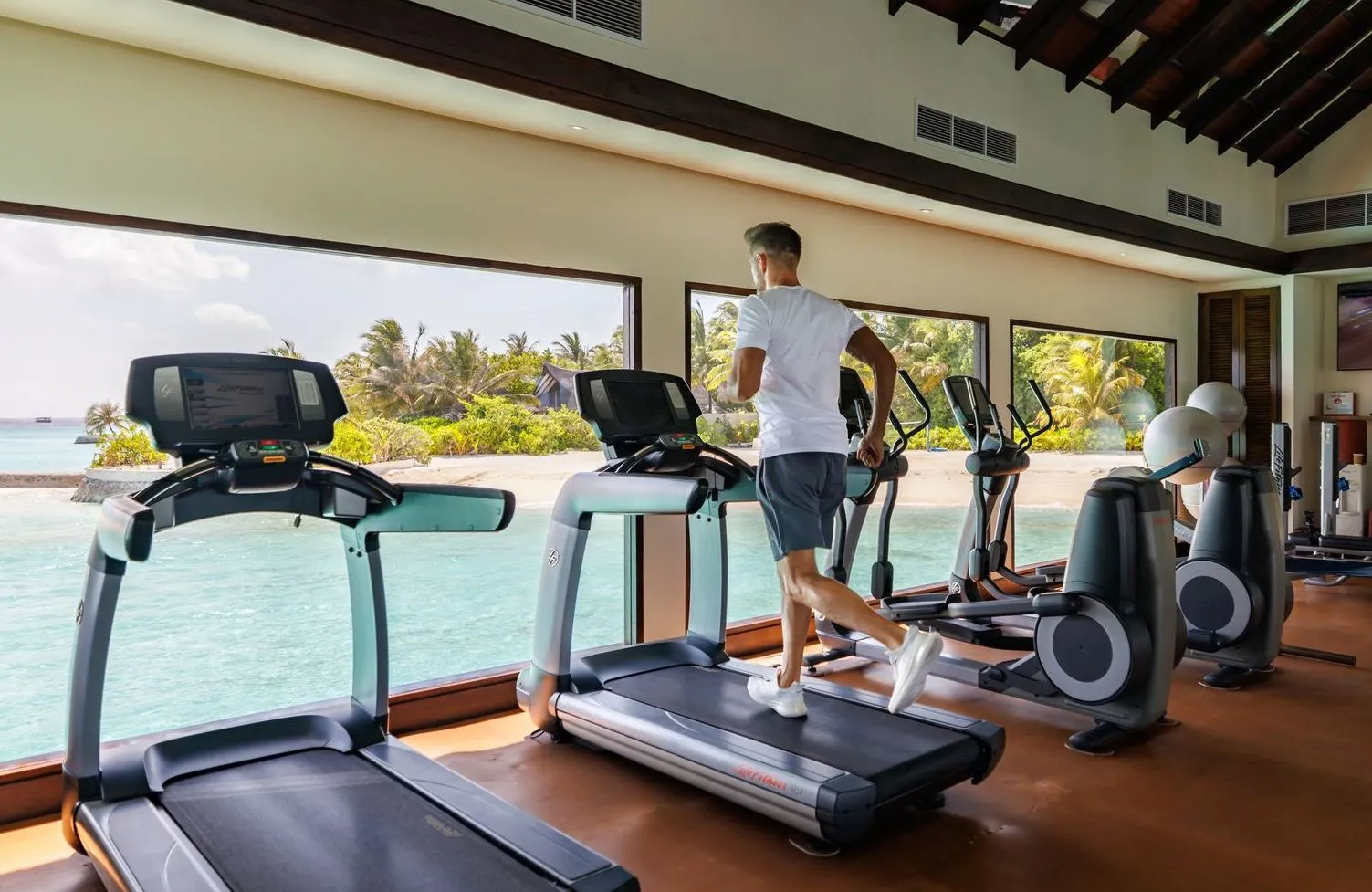The overwater gym, a guest on a treadmill facing the windows over the lagoon.