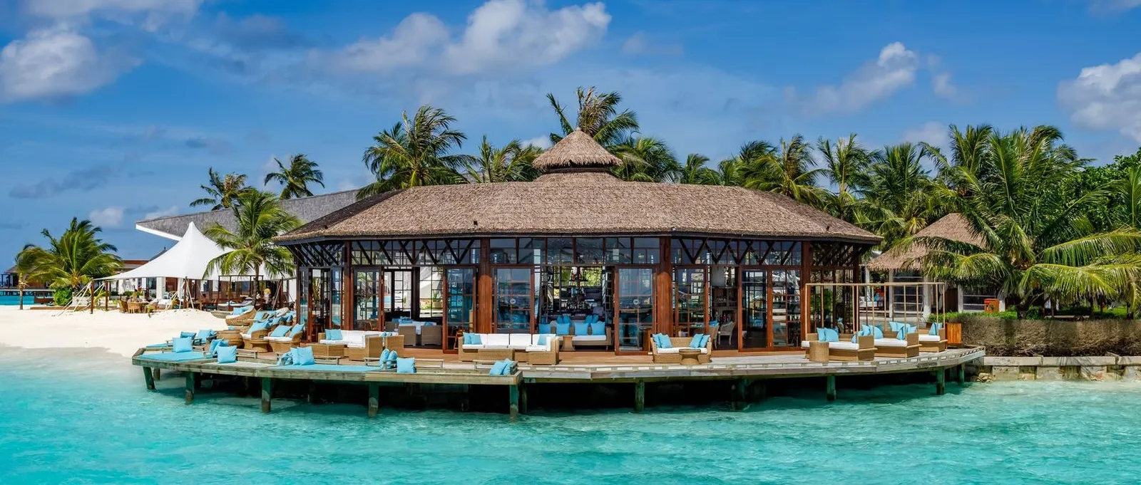 OZAR, the bar on a platform over the lagoon, its blue sofas on the deck and palms behind.