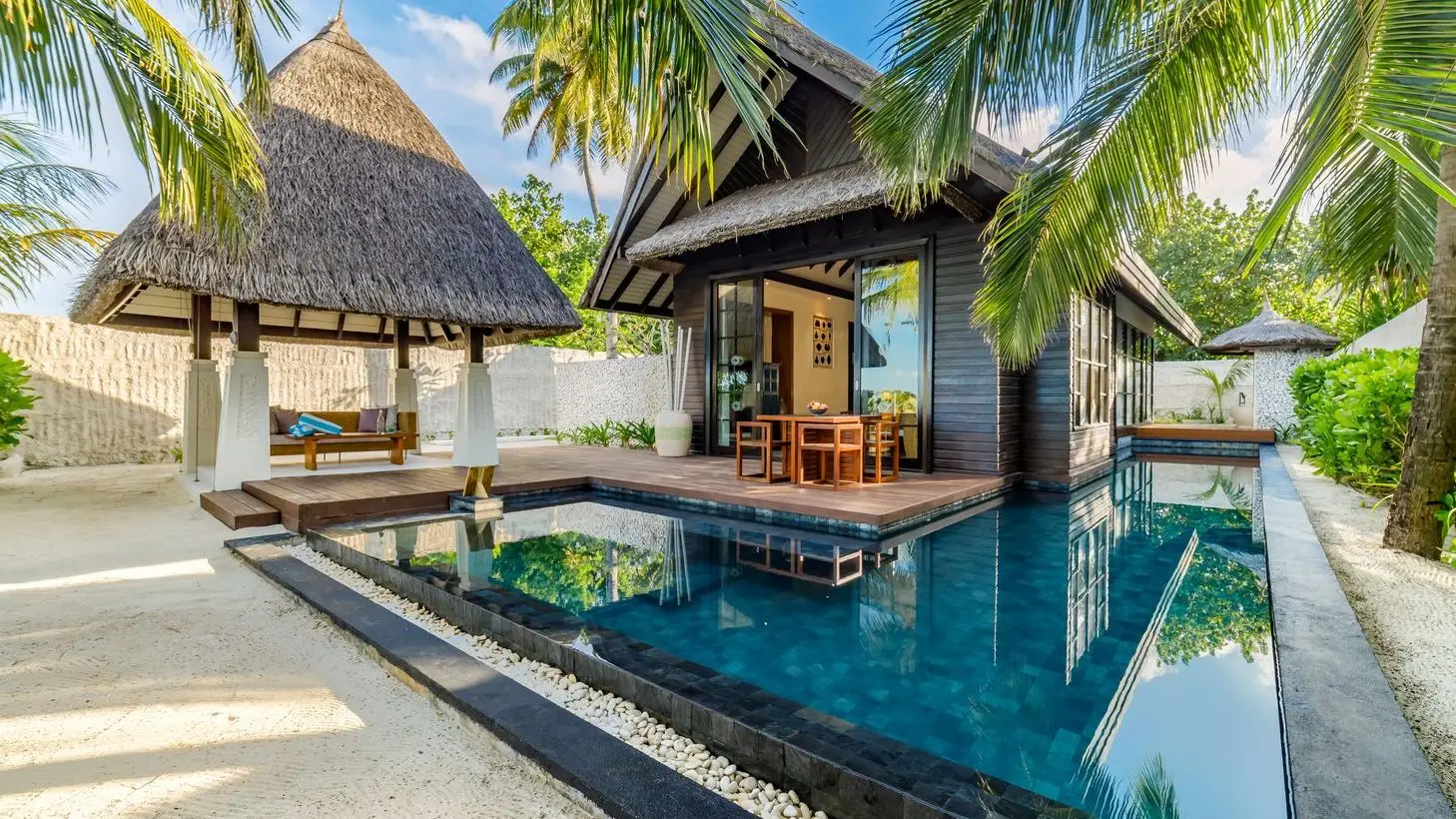 An Earth Pool Villa: the L-shaped pool in front of the thatched villa, its pavilion and the palms.