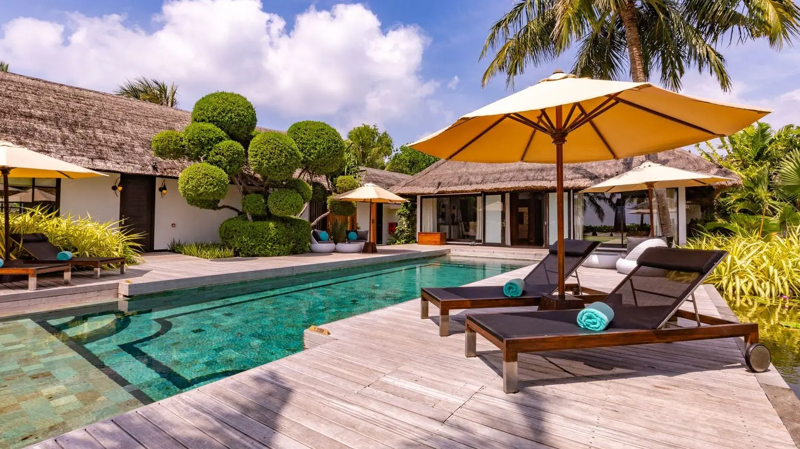 The Royal RESERVE’s pool, with loungers, parasols and the thatched pavilions in the garden.