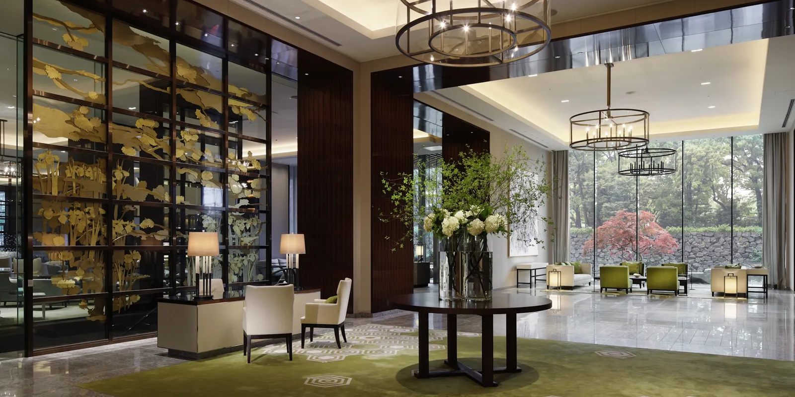 The lobby: a large vase of white flowers on a round table, armchairs and tall windows onto the trees.