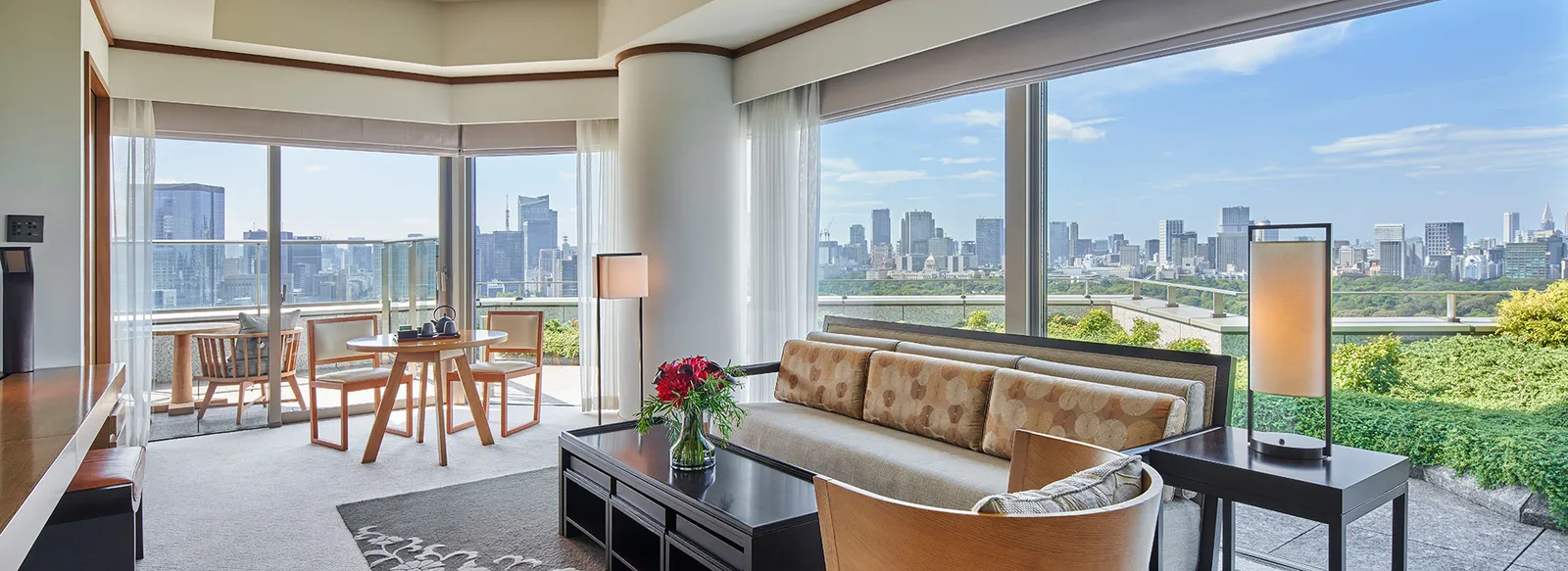 The top-floor Chiyoda Suite’s living room: the upholstered bench, a table with roses and the windows over the gardens and the towers.