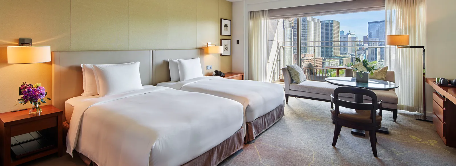A twin room by day with the seating area by the window and the Marunouchi towers outside.