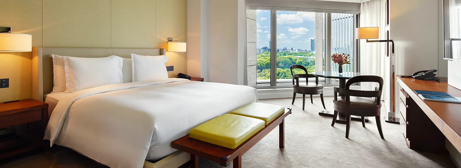 A Deluxe room with a king bed: the green bench at its foot, a small table with 2 chairs and the window onto the gardens.