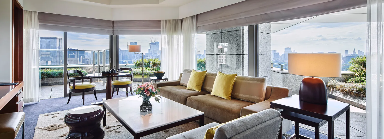 The Garden Suite’s living room, with its yellow-cushioned sofas and the corner windows onto the balcony and the city.
