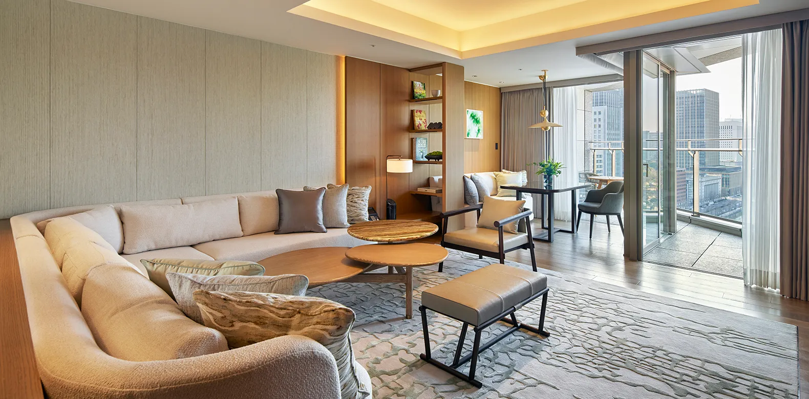 The Premier Suite’s living room, with its curved sofa, round tables, pale wood and the door to the balcony.