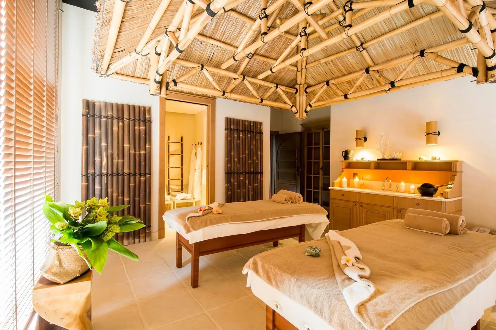 A Grand Spa treatment room in Balinese style: 2 massage beds, a ceiling of bamboo canes and candles lit on the cabinet