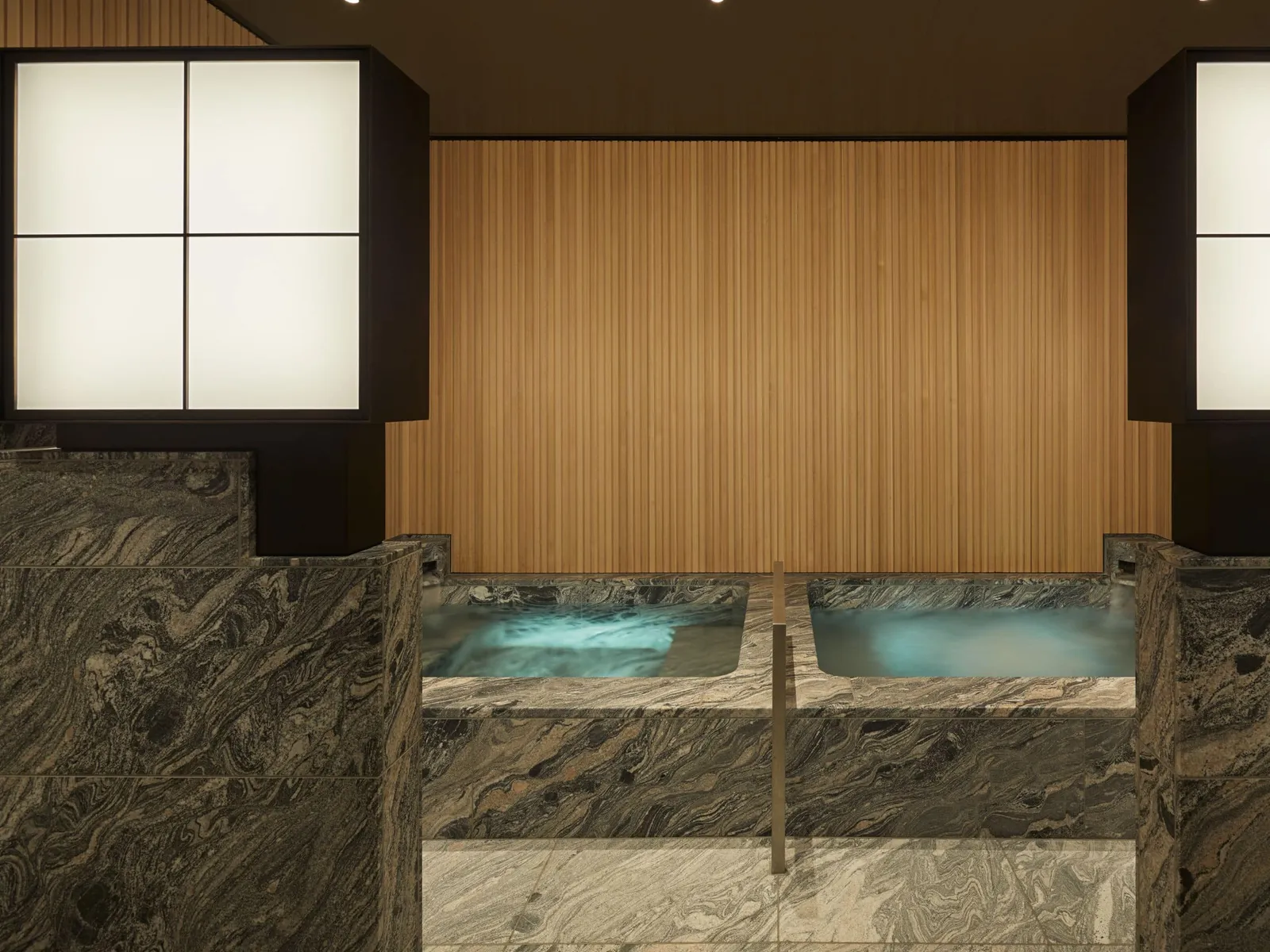 The Bath House: 2 baths in dark veined stone, pale timber walls and 2 paper lamps.