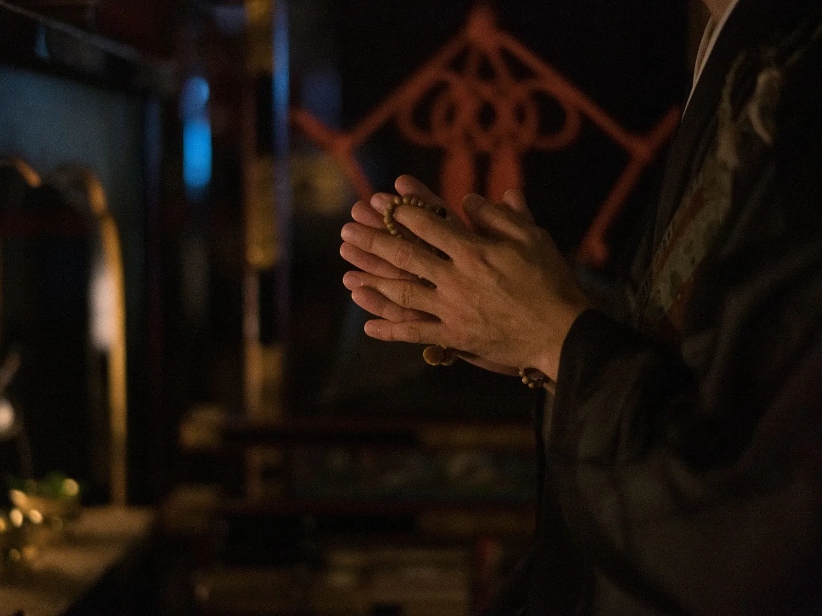 2 hands joined around a Buddhist rosary, in the half-light of Kiyomizu-dera.