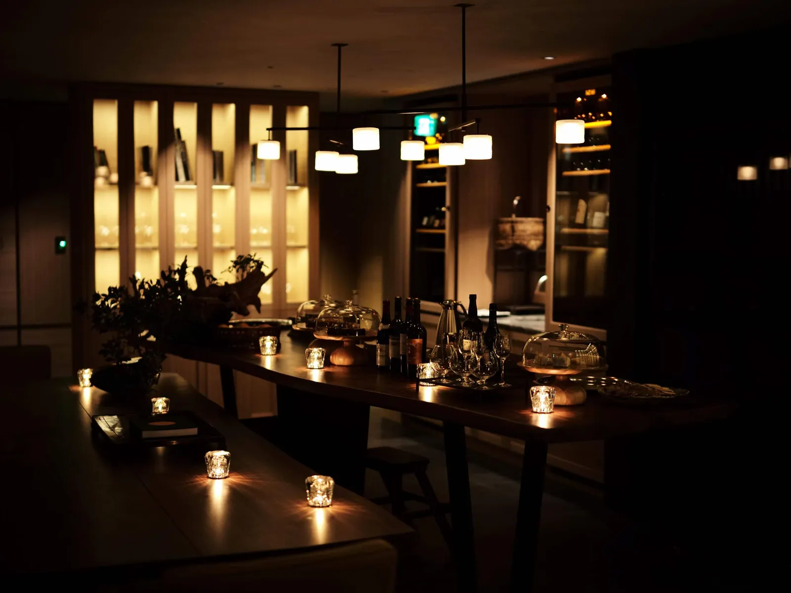 The Living Room at night: the long table with candles, bottles lit on the shelves.