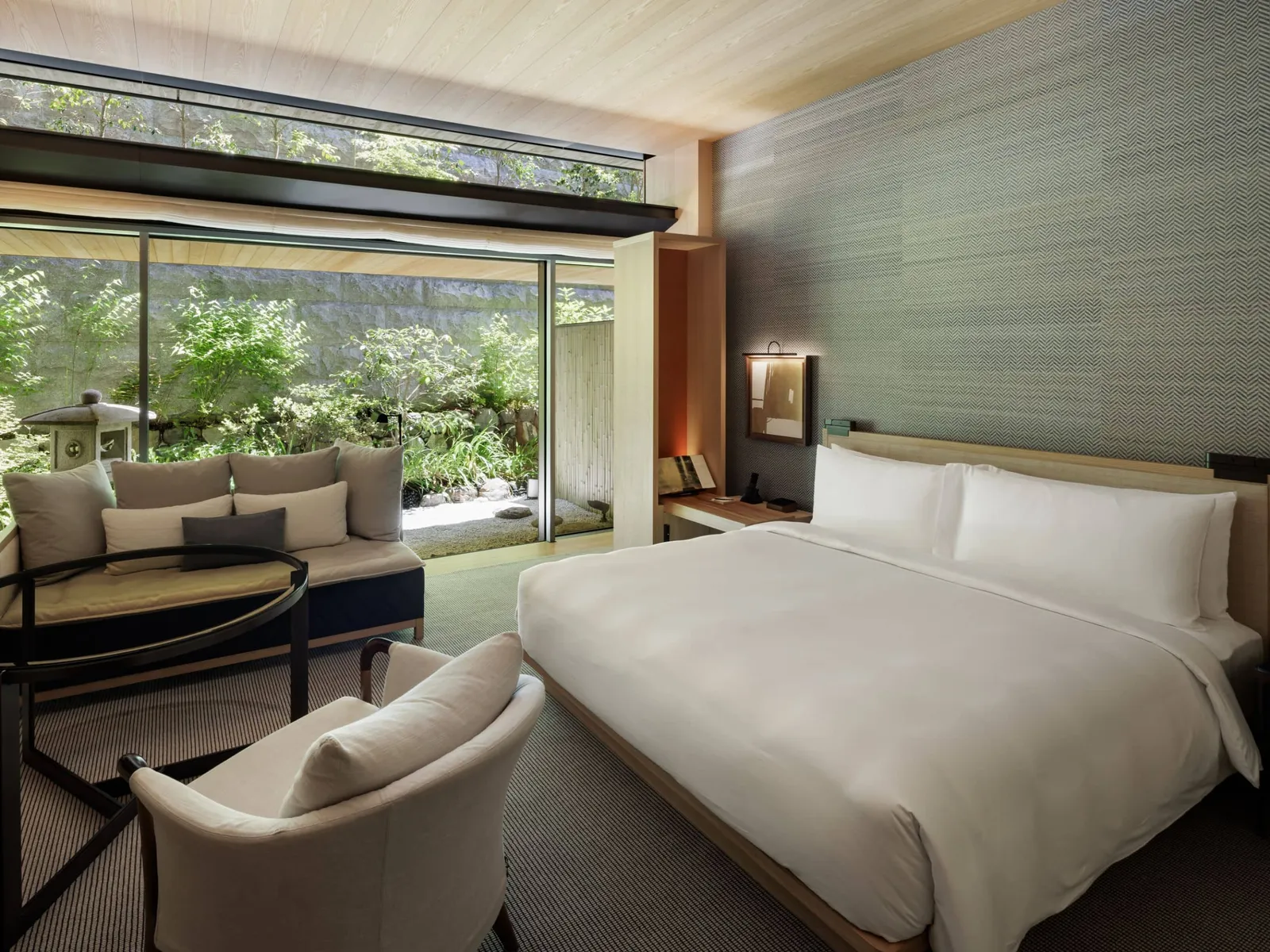 A 45 m² king room with a sofa and an armchair, and the glass wall onto a garden with a stone lantern.