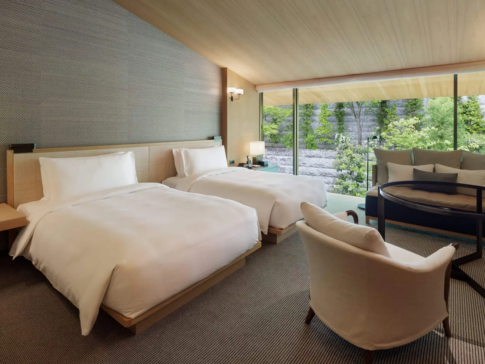 A 45 m² twin room, its round table and the glass wall onto the green of the hillside.