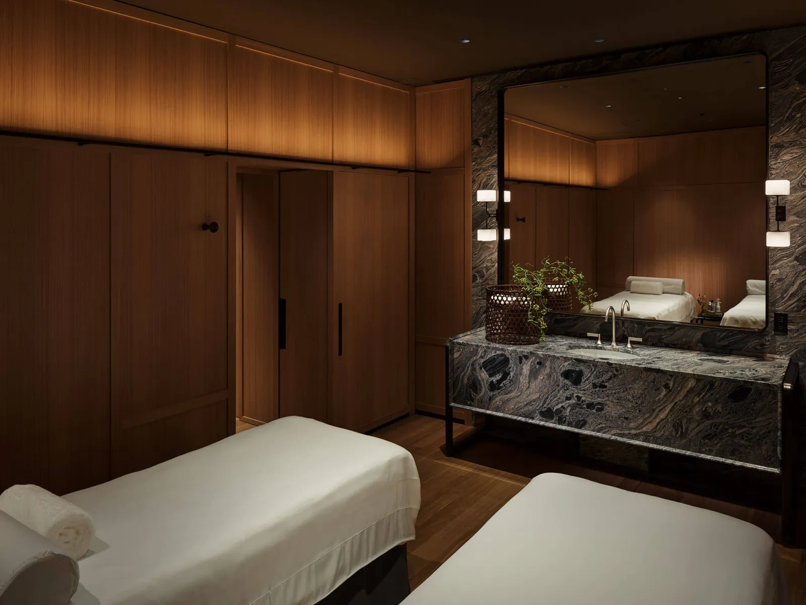 A treatment room with 2 beds, timber walls and a basin in dark marble.