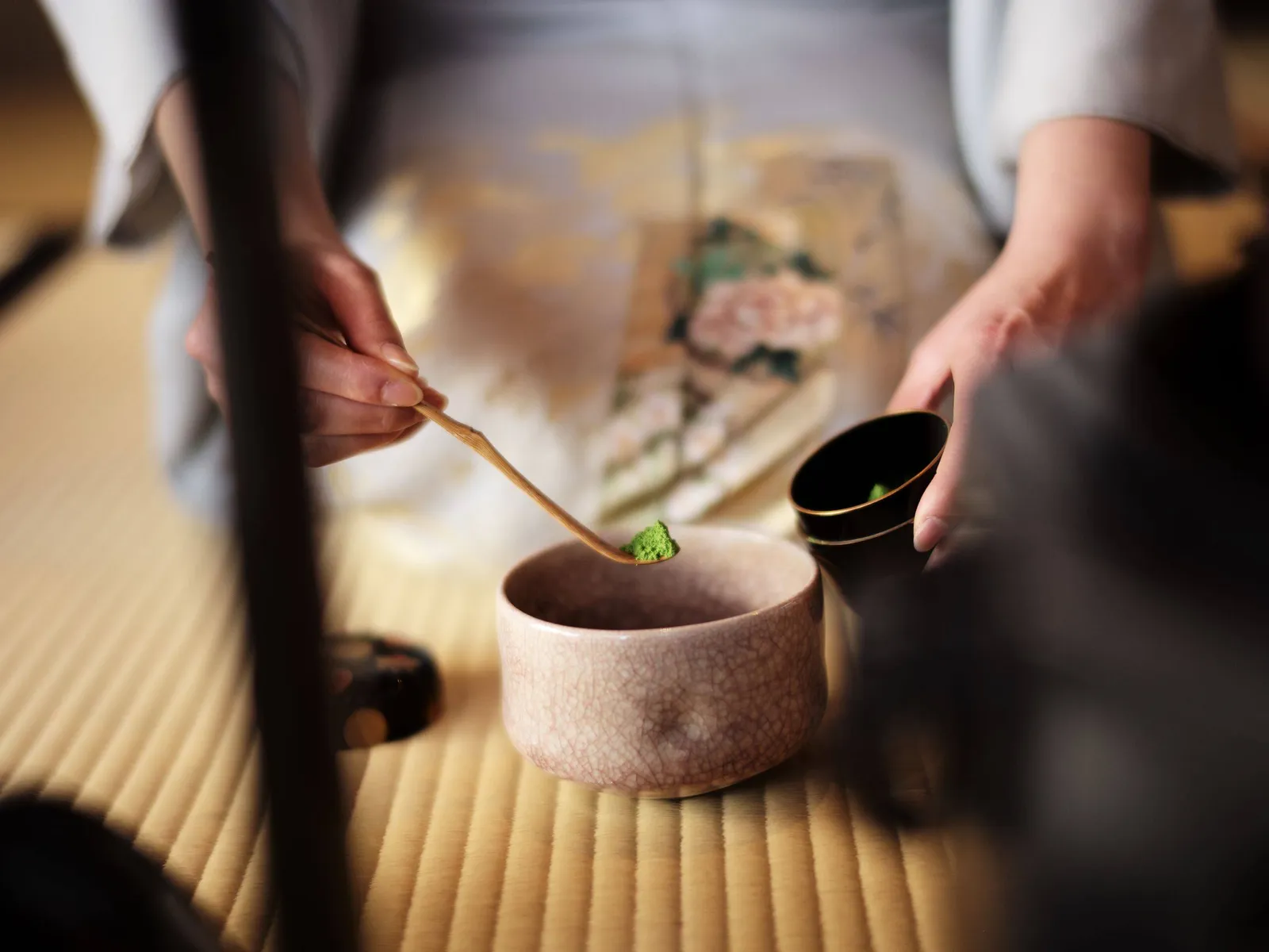 The hands of a tea master: the bamboo scoop above the bowl, on tatami.