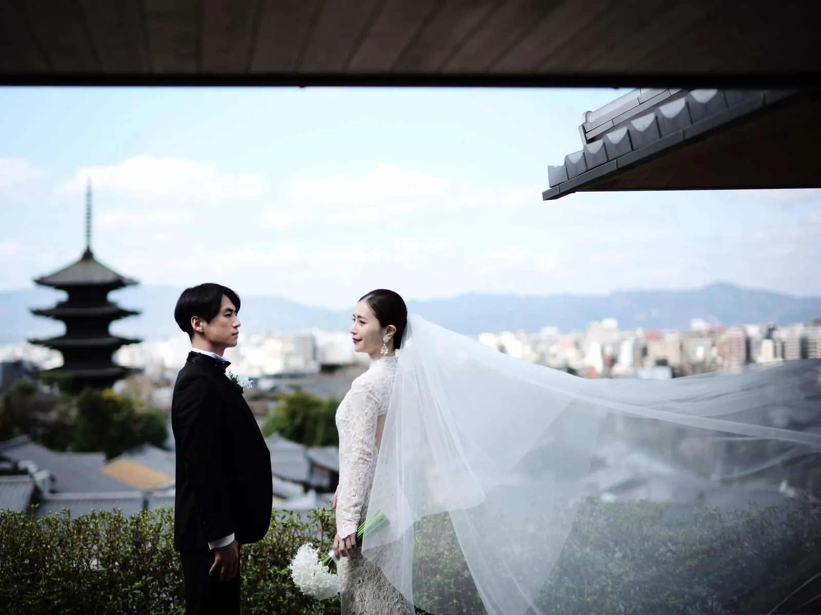 A bride and groom on the terrace, he in a morning coat and she with her veil in the wind, the pagoda behind.