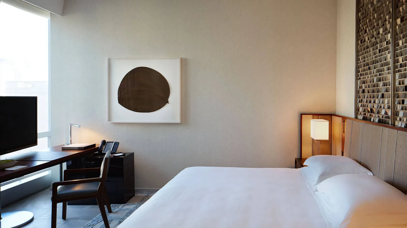 King bed with grey headboard, window-side desk and circular wall art