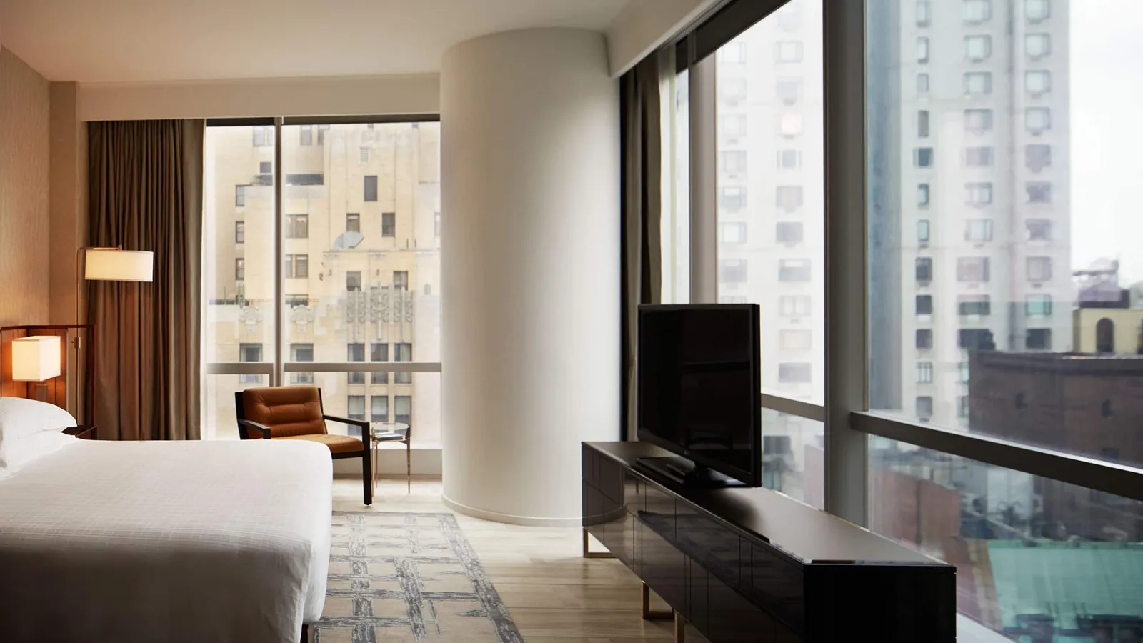 King bed and armchair between corner windows overlooking the city