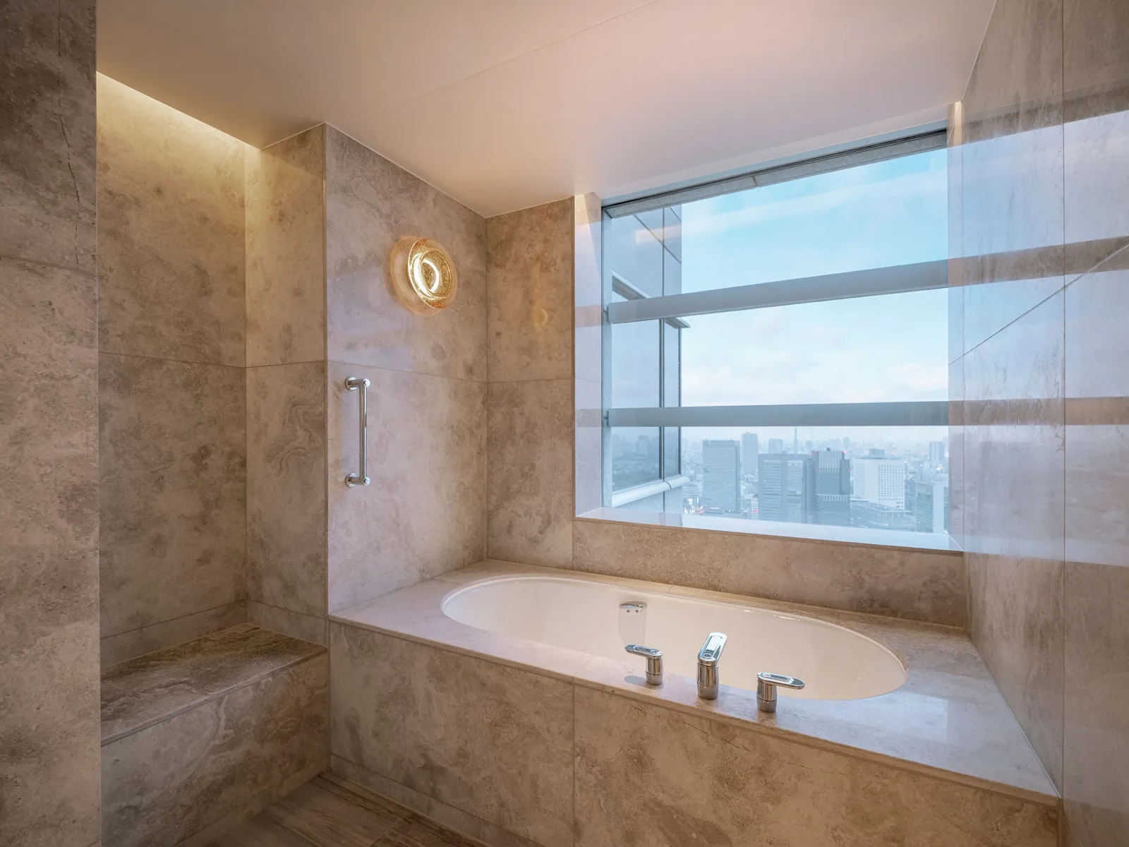 The Corner Premium bathtub under the window, between marble walls, with the towers outside.