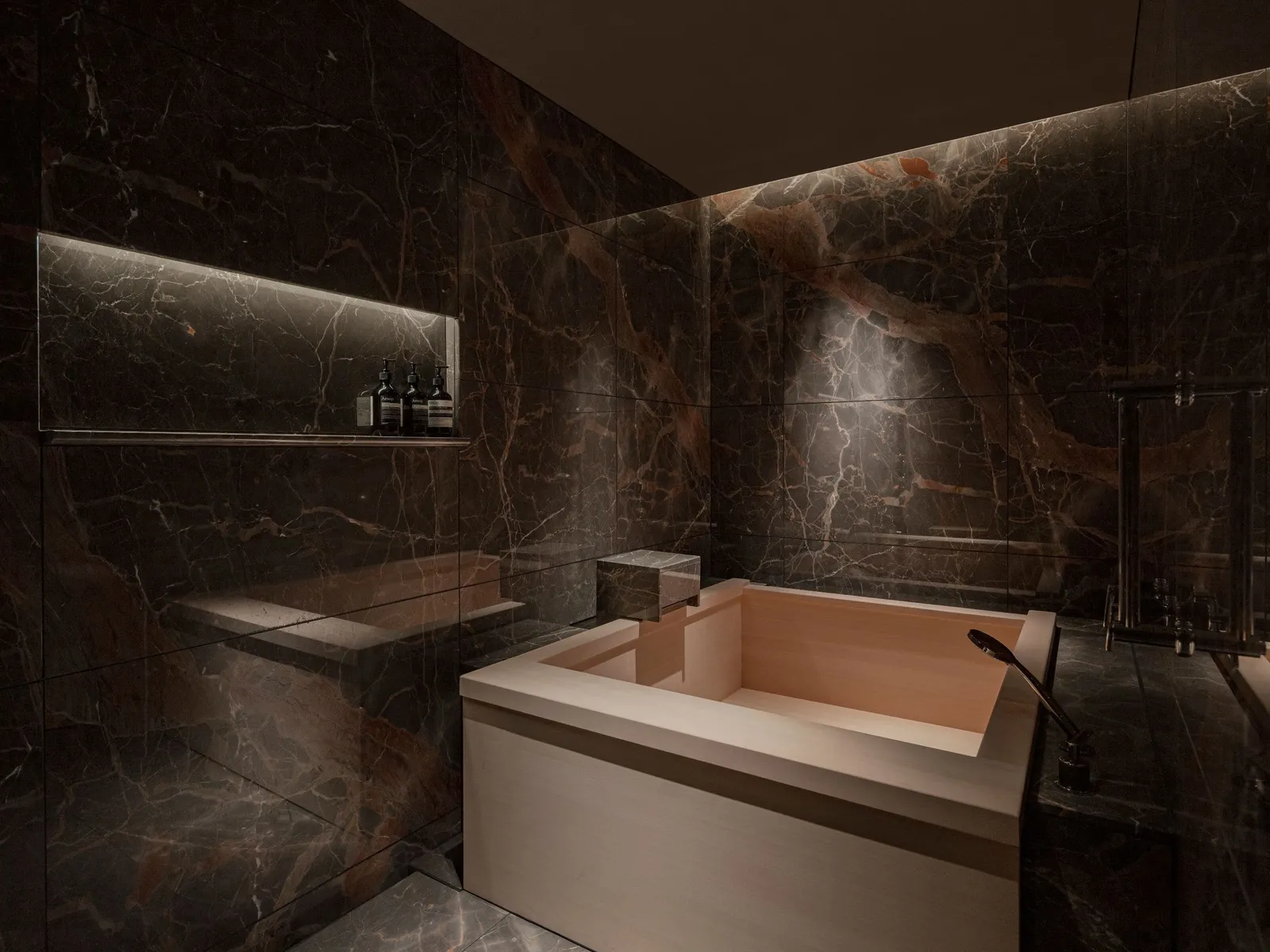 The Governor’s Suite hinoki wood bathtub between dark marble walls.