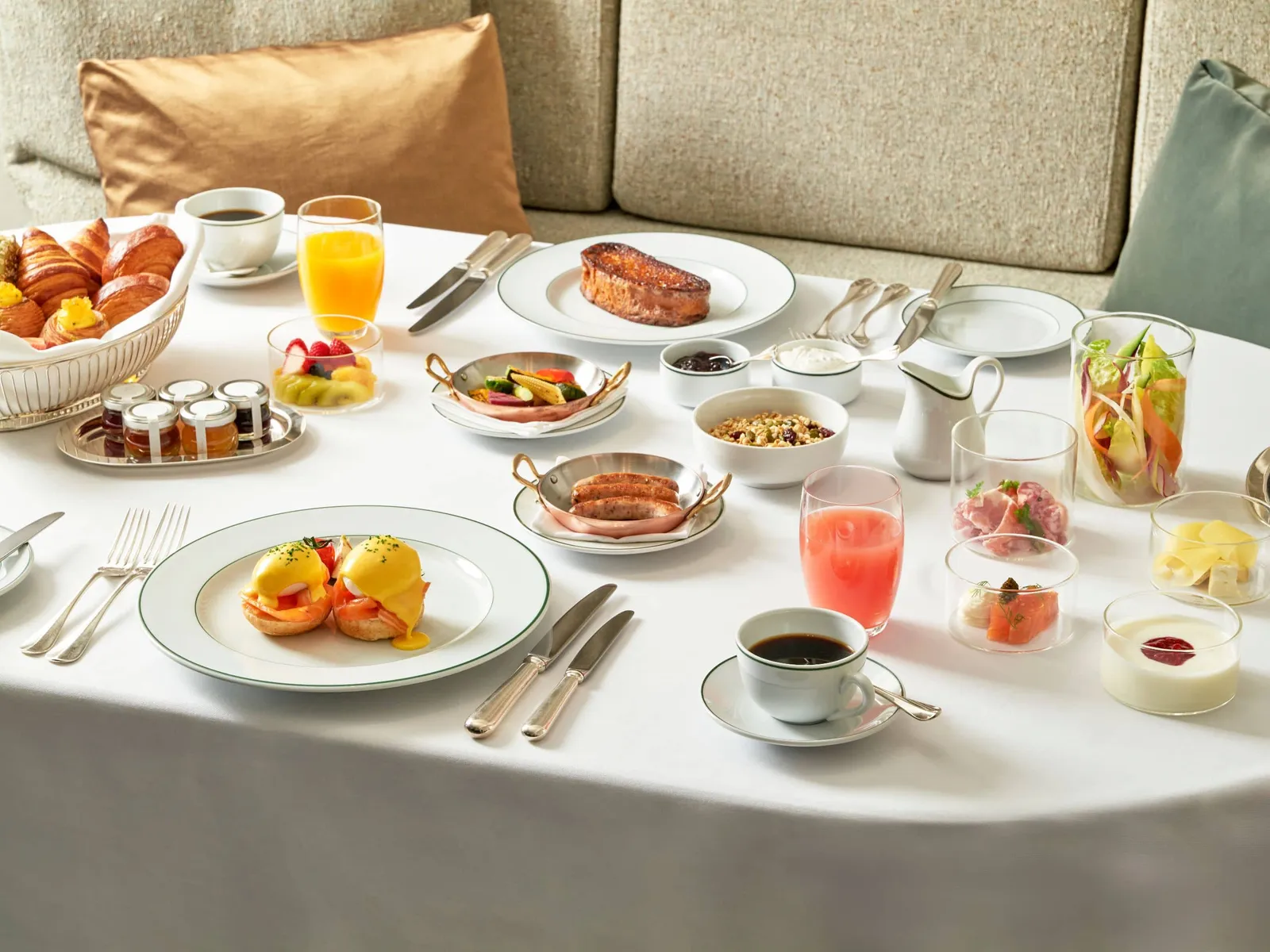 Breakfast served in the room: eggs Benedict, croissants, fruit, juices and coffee on a white tablecloth.