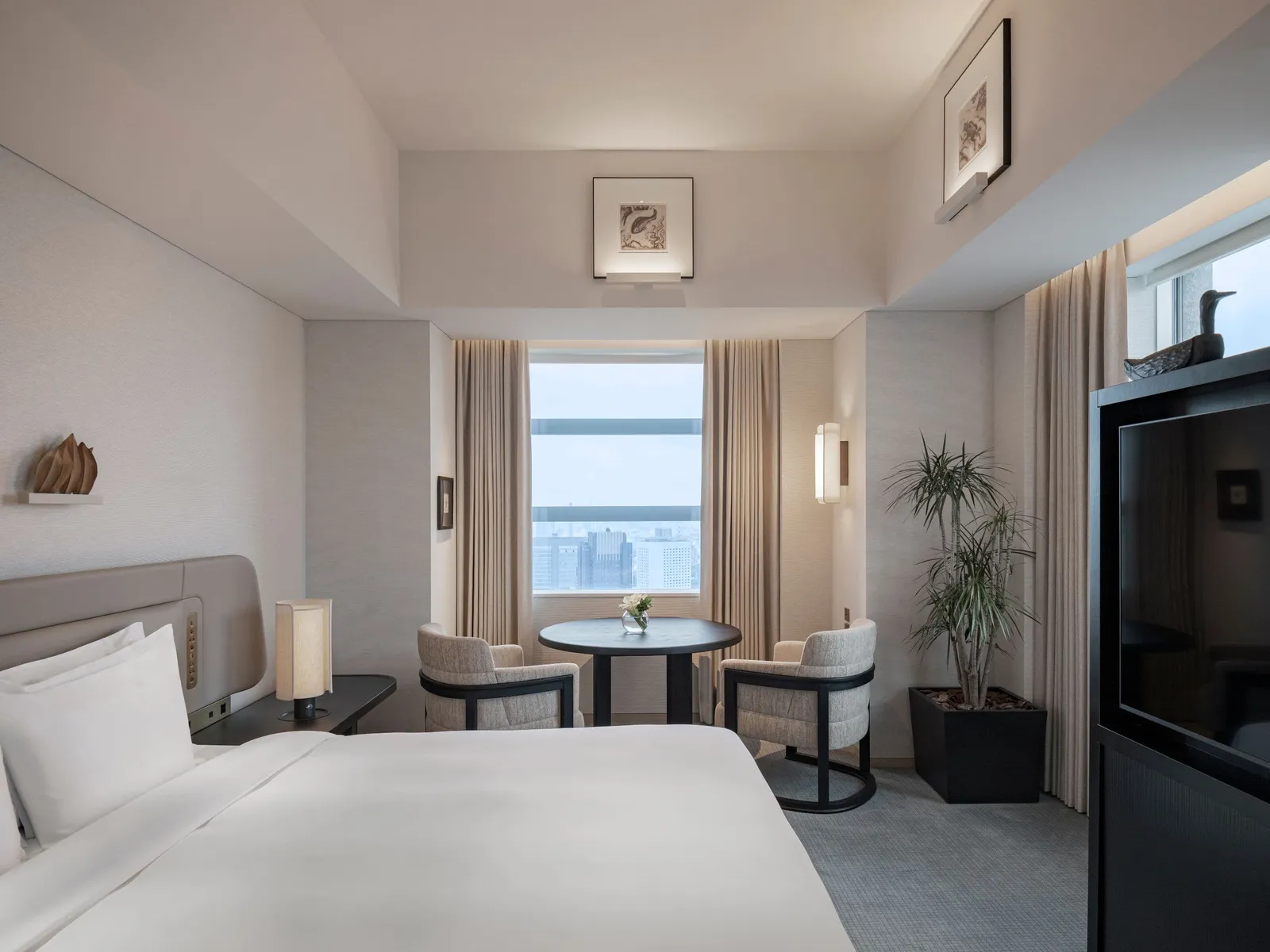 The Corner Premium: the bed, a small table with 2 armchairs under the window and a potted plant.