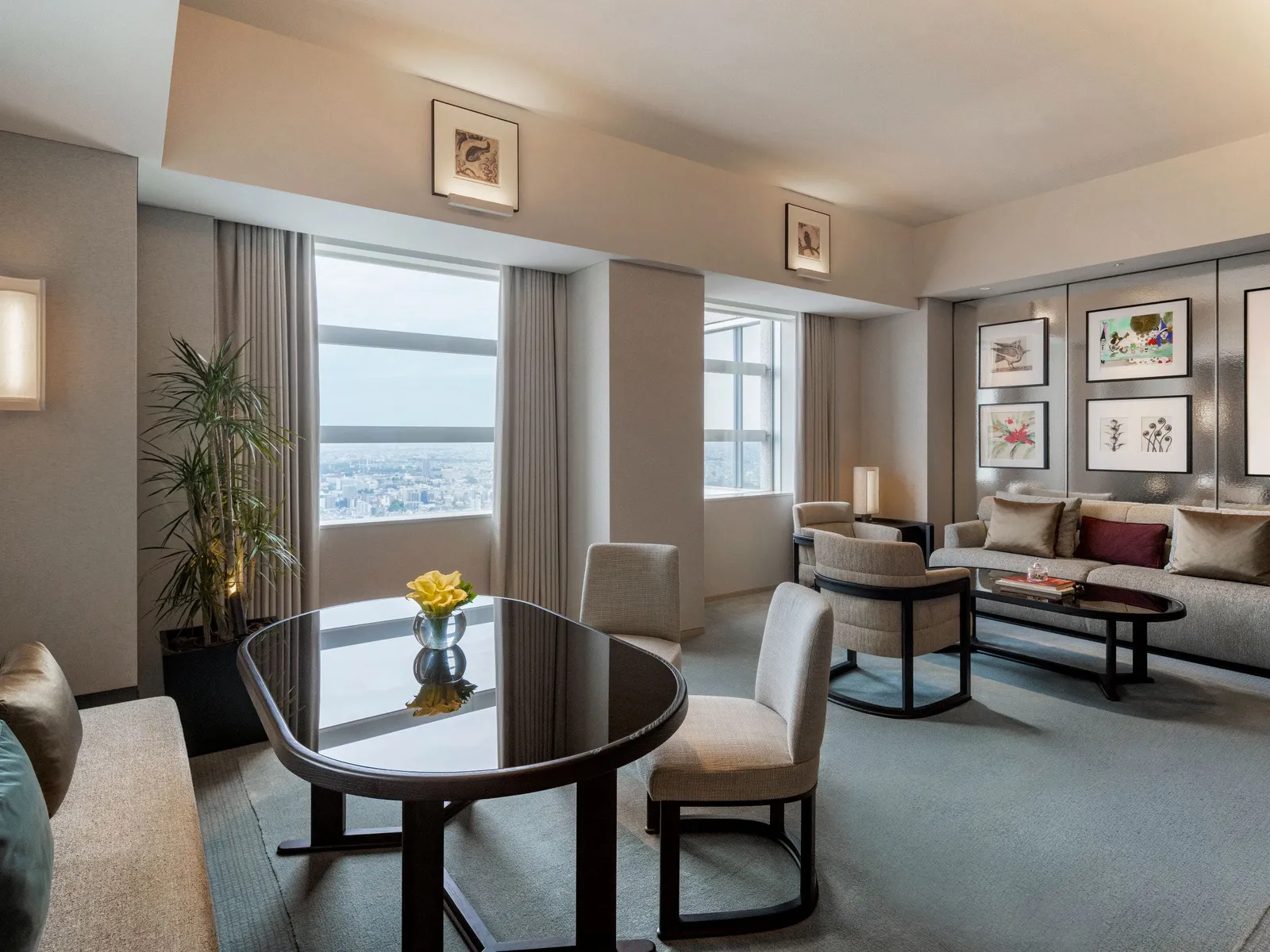 The Park Deluxe Suite living room: the sofa, the oval dining table with flowers and 2 windows onto the city.