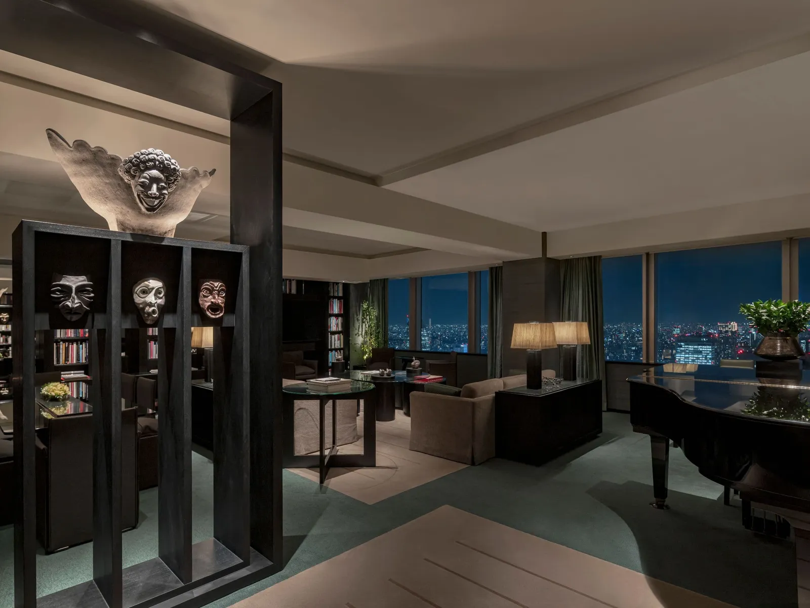 The Tokyo Suite at night: masks on a bookcase, the grand piano and the windows onto the city lights.