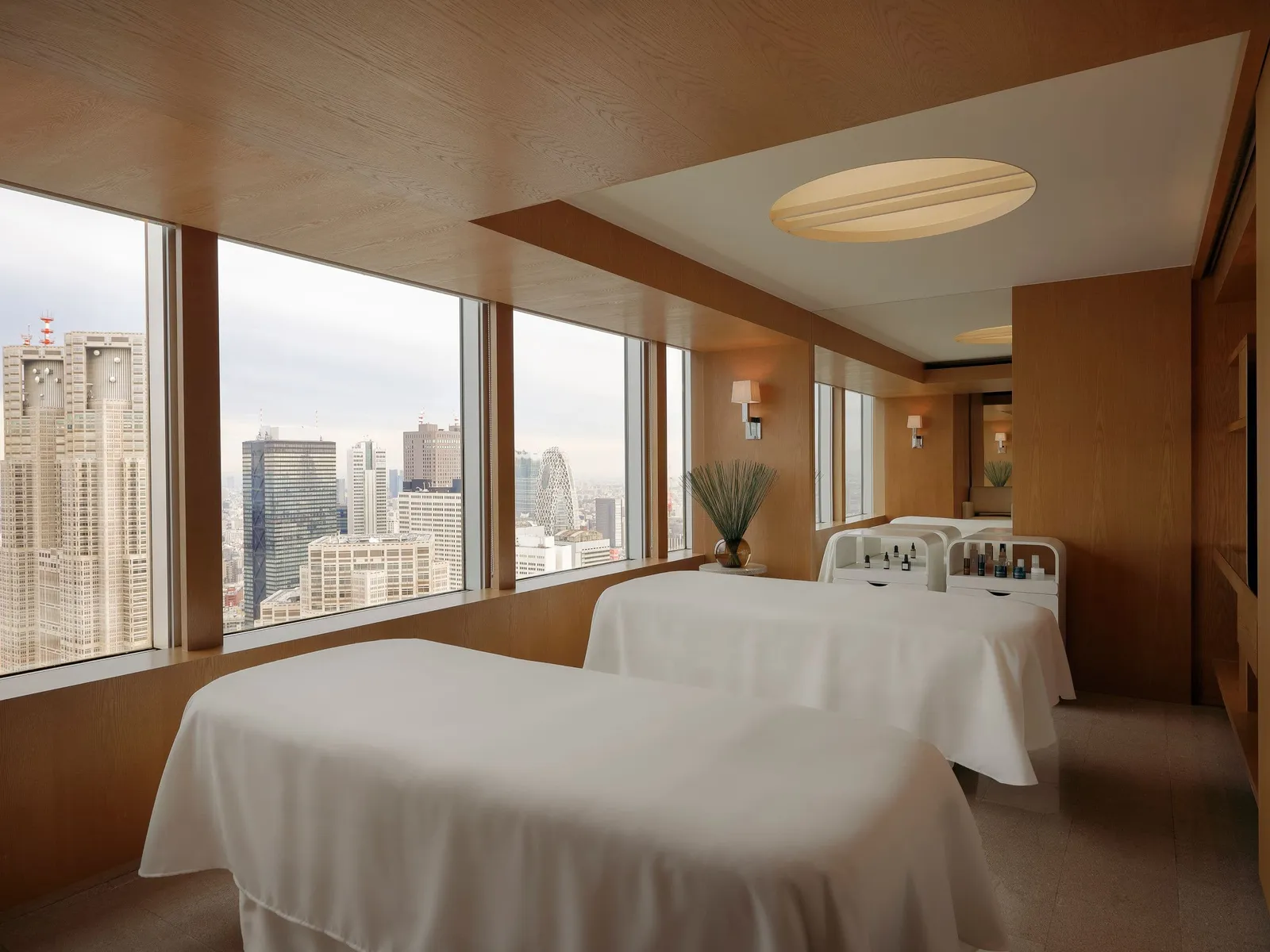 A treatment room with 2 massage beds and windows onto the towers, among them the Tokyo Metropolitan Government Building.