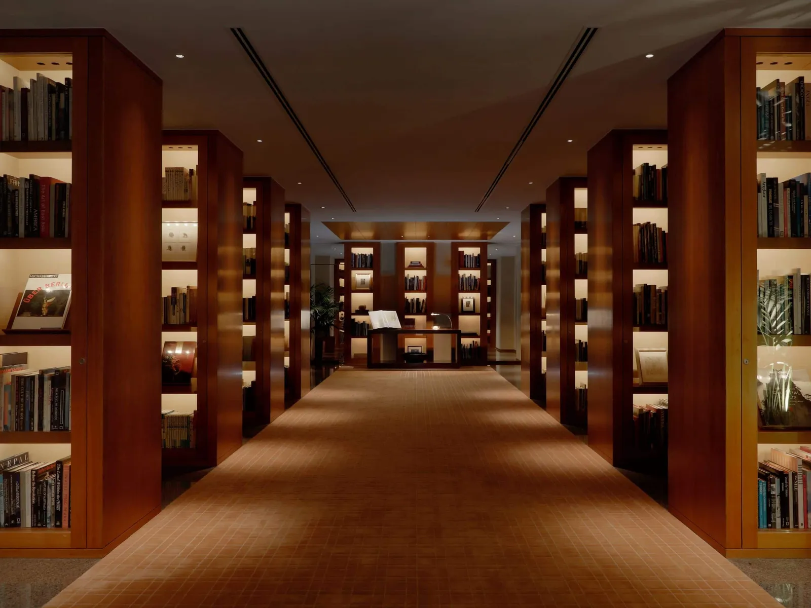 The Library on the 41st floor: a long carpeted corridor between 2 rows of wooden shelves of lit books.