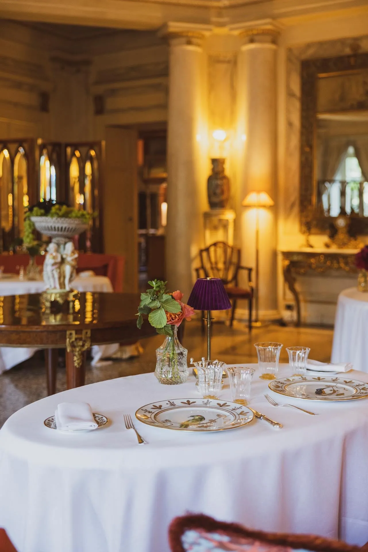 A round table laid in the Sala Ovale under a chandelier, wood panelling and bookcases behind