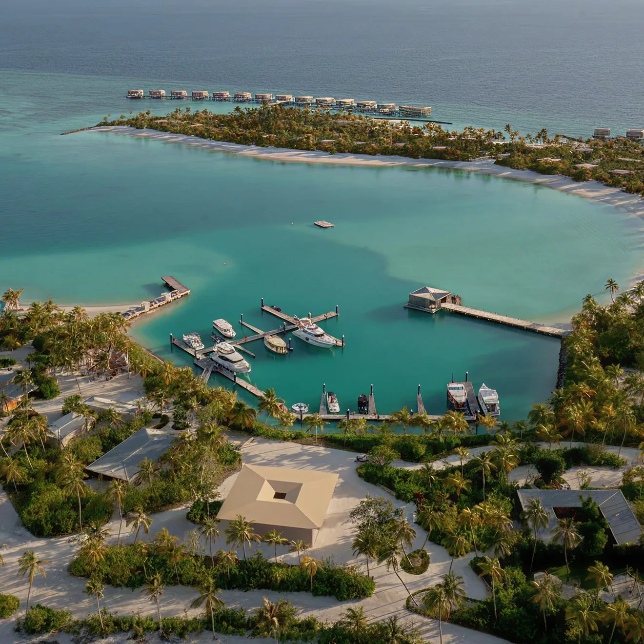 The island from the air: the marina and its moored boats, the turquoise lagoon and the water villas beyond