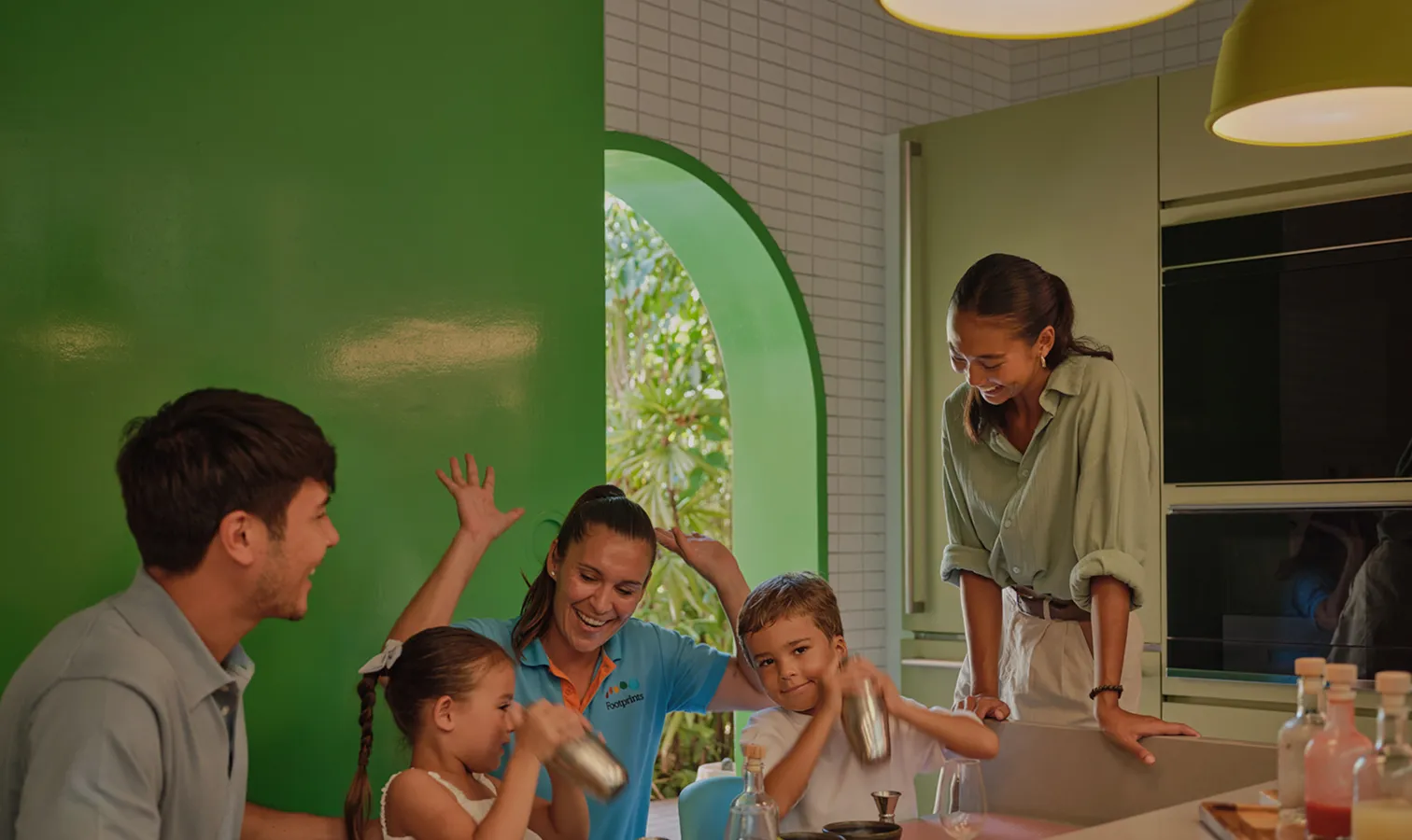 Children and adults playing round a table, in front of a green wall with an arch