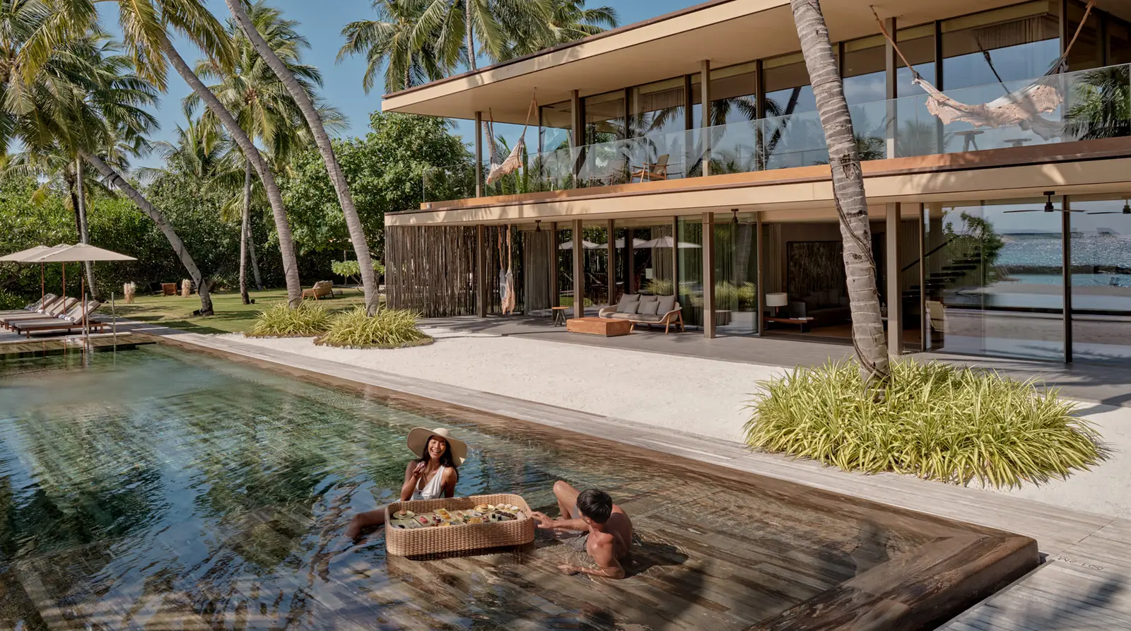 The 2-storey Beach House, its long pool in front and 2 guests in the water with a floating tray