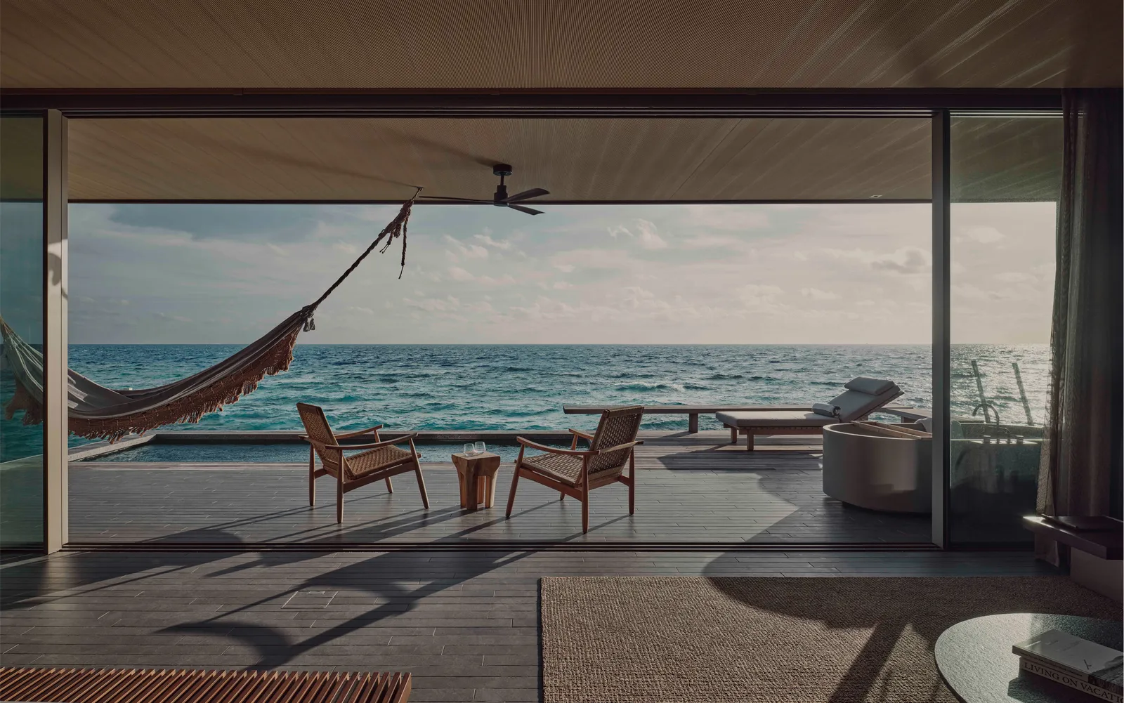 A water villa open onto its deck: the hammock, 2 chairs and the ocean to the horizon