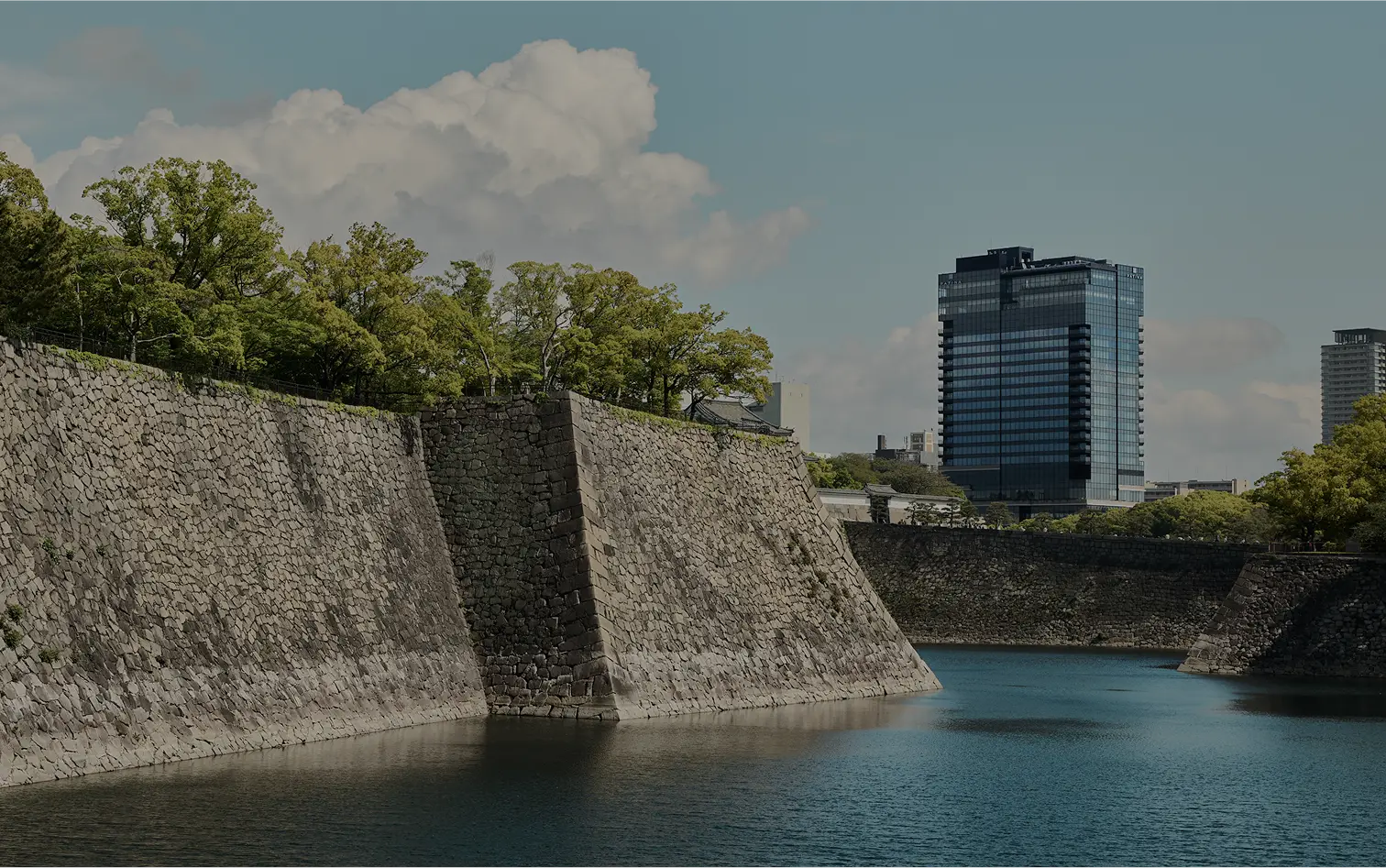 The stone walls and moat of Osaka Castle, the hotel’s glass tower rising beyond the trees