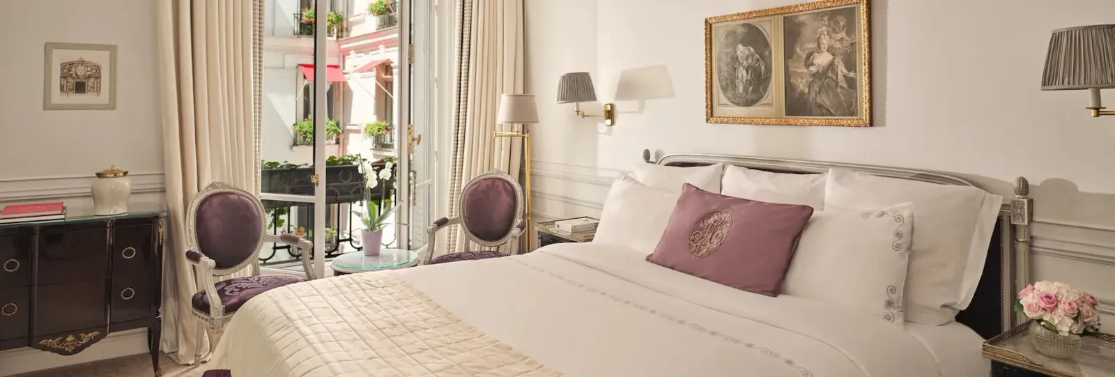 A bedroom with a bed, 2 purple chairs, a desk and French doors