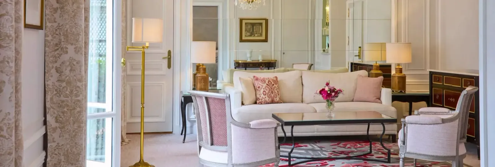 A sitting area with a pale sofa and armchairs, glass coffee table and lamps