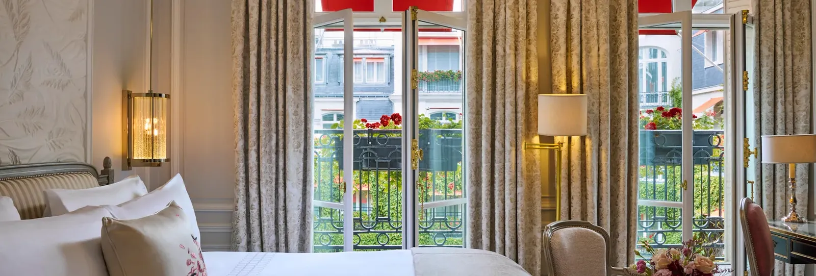 A bedroom with a bed, French doors and flowers along the railings outside