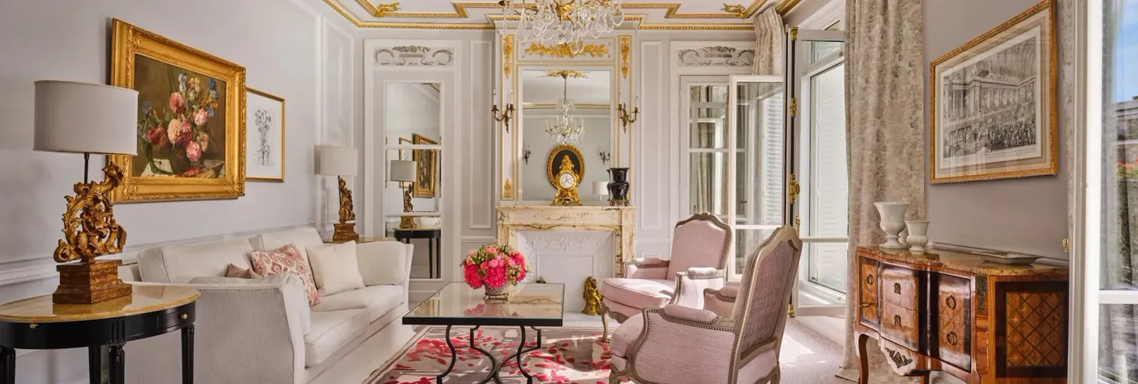 A living room with a fireplace, gilded mirror, pale sofa and pink seating