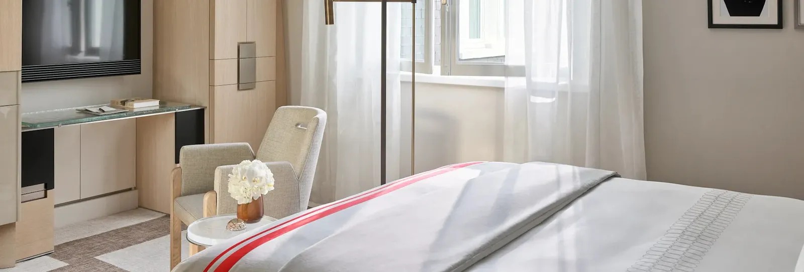 A bedroom with a bed, wall-mounted television and a pale armchair beside the window