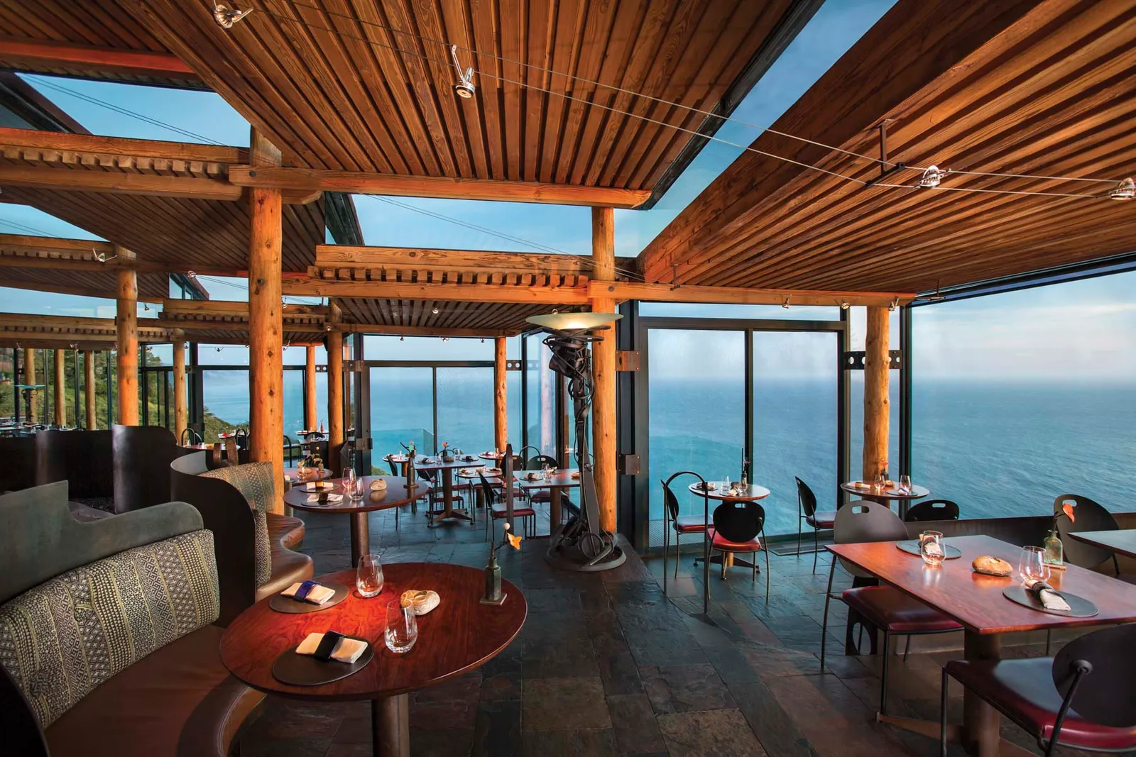 Sierra Mar’s empty dining room, with tables laid, a slatted timber ceiling and glass walls onto the Pacific.