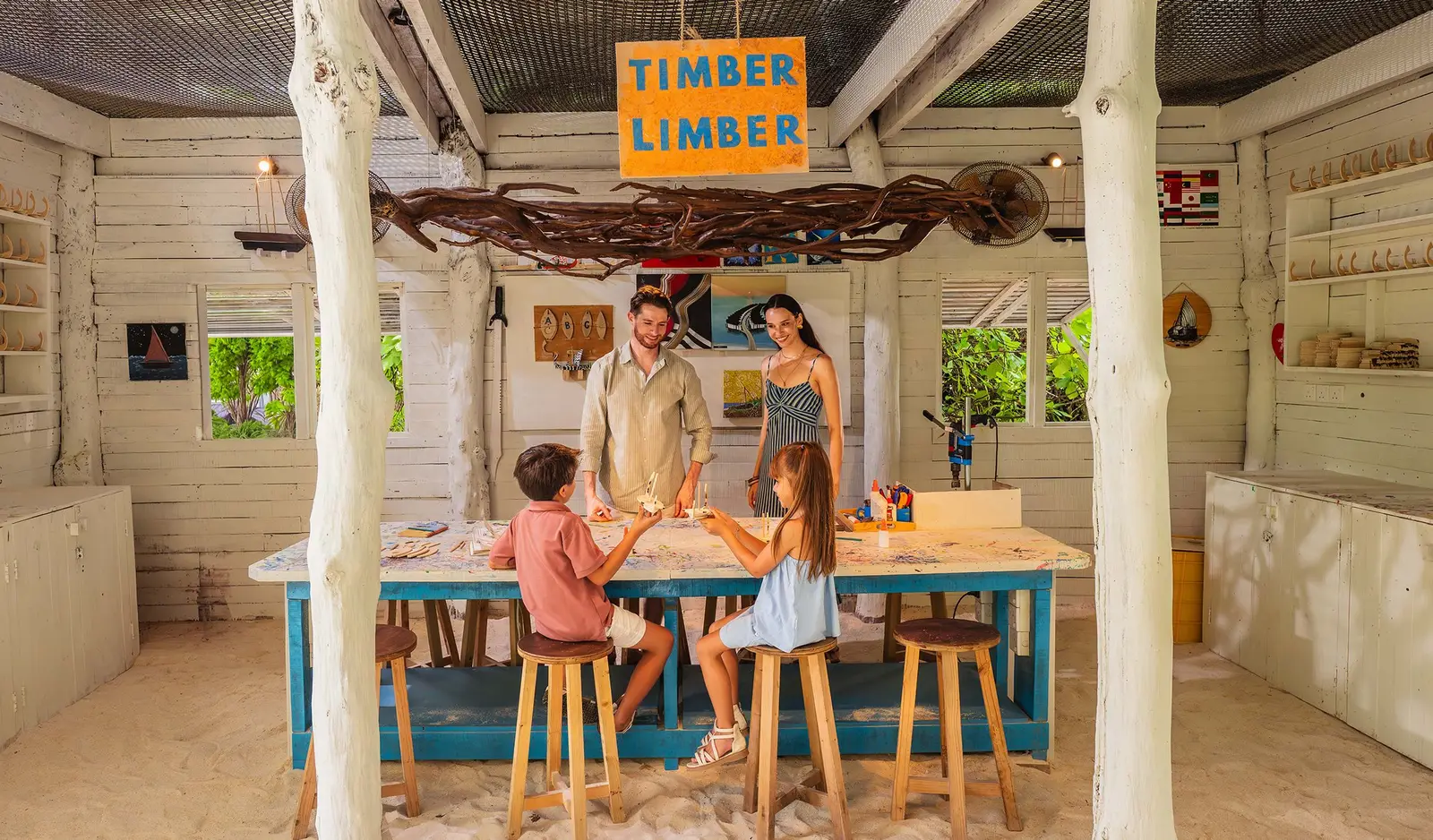 A family at the Artist Zone’s counter, under the «Timber Limber» sign, building small wooden boats.