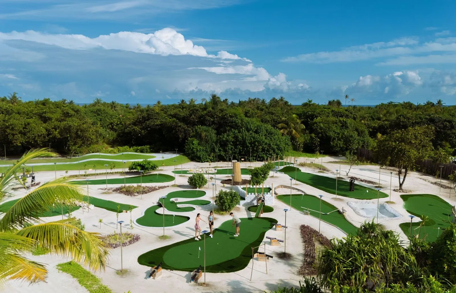 The mini-golf course among sand and greenery, its holes on artificial lawns and the forest behind.